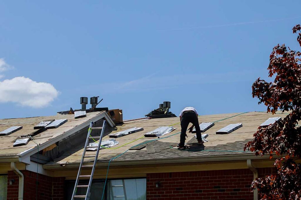 A construction worker installing synthetic roof underlayment on a wooden roof deck before laying shingles.