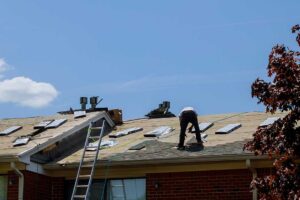 A construction worker installing synthetic roof underlayment on a wooden roof deck before laying shingles.