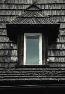 Attic roof framing shows condensation droplets, damp insulation, and dark moisture stains on the wood deck.